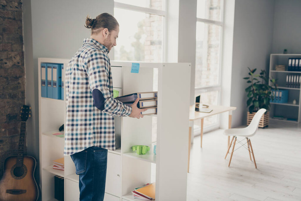 Profile photo of young business guy new company trainee administrator manager help boss with folders documents shelf organizing wear casual shirt jeans home office indoors - 写真・画像