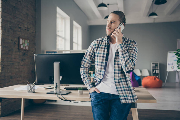 Photo of handsome business administrator guy leaning table self-confident person talking telephone with partners wear casual shirt standing spacious modern interior office indoors - Фото, изображение