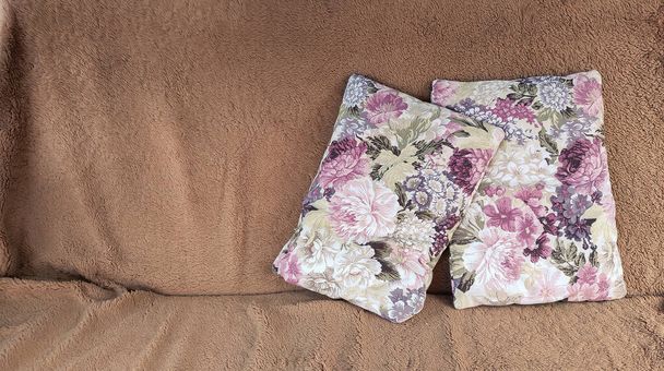 két nyomtatott lila virág párnák a barna kanapén a dácsa, pihenés és kikapcsolódás - Fotó, kép