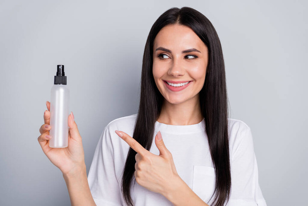 Portrait of positive cheerful girl promoter try new hygiene dispenser indicate point index finger wear white t-shirt isolated over gray color background - 写真・画像