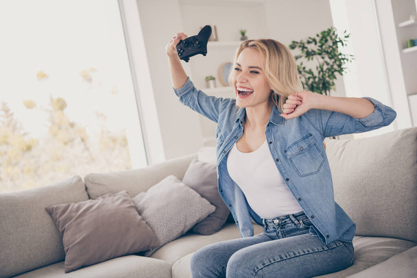 Profile photo of cheerful lady sitting comfy couch positive emotions playing video games stay home quarantine time addicted gamer raise hands fists win victory living room indoors - 写真・画像