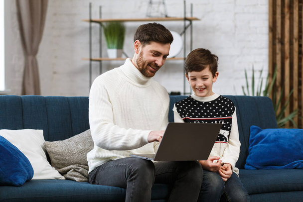 Stay home. Portrait of smiling father and son using laptop for a online meeting, video call, video conference with relatives, home education. Happy family spending time together at home - Fotoğraf, Görsel