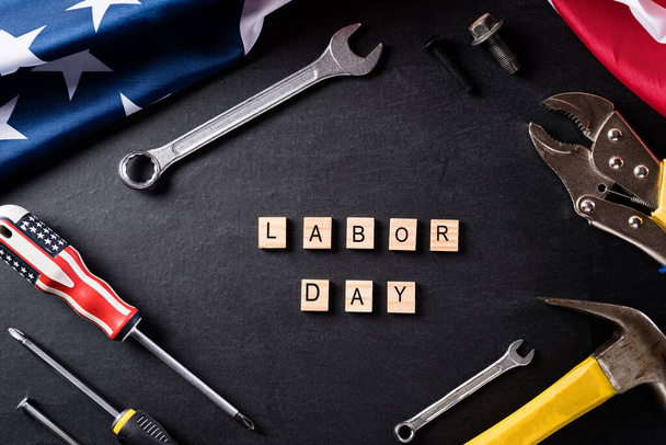 Happy Labor Day concept. Amerikaanse vlag met verschillende bouwgereedschap op zwarte tafel achtergrond, met Labor Day tekst. - Foto, afbeelding