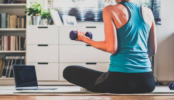 Home Workout-Konzept Frau im Wohnzimmer mit Laptop und Hanteln psychische Gesundheit in Quarantäne - Foto, Bild