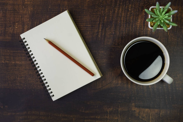 Top view of open school notebook with blank pages, red pencil, Plant and Coffee cup on wooden table background. Business, office or education concept with copy space. - 写真・画像