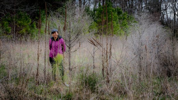 Femme au chapeau et manteau violet debout au milieu de la broussaille dans une forêt à côté d'un chemin dans le comté d'Orange, Caroline du Nord
 - Photo, image