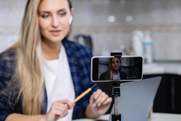 Vrouw blogger is het opnemen van video op de smartphone in het huis keuken interieur. Coronavirus quarantaine, sociale afstand, particuliere ondernemer. - Foto, afbeelding