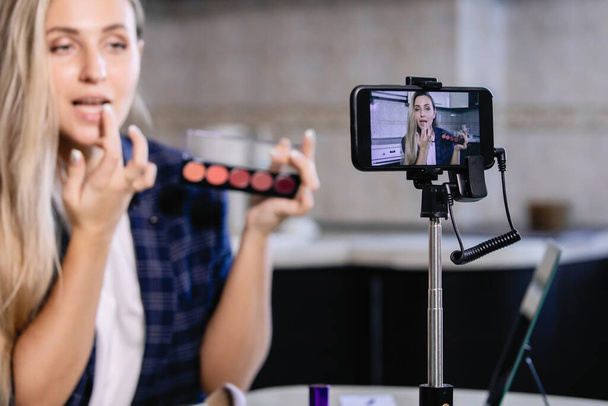 Vrouwelijke blogger demonstreert een set lippenstift op een smartphone. Coronavirus quarantaine huiswerk, sociale afstand, particuliere ondernemer. Geselecteerde focus. - Foto, afbeelding