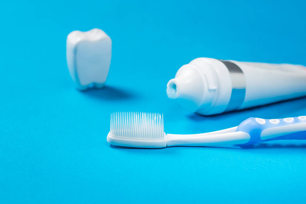 Eine Zahnfigur, eine Tube Zahnpasta und eine blaue Zahnbürste mit Silikonborsten auf blauem Hintergrund. - Foto, Bild