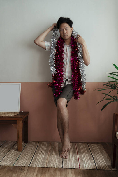 Wspaniały azjatycki gej stojący z palcem wskazującym na ścianę z czerwonym i srebrnym świecidełkiem. - Zdjęcie, obraz