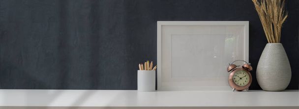 Plan recadré d'un lieu de travail moderne avec un cadre maquillé et des fournitures de bureau sur une table blanche et un mur gris
  - Photo, image