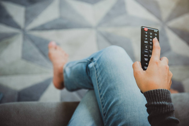 Top view of young woman holding remote control and turning on the TV while sitting on sofa at home. Stop the virus Covid-19.Stay at home Concept. - Photo, Image