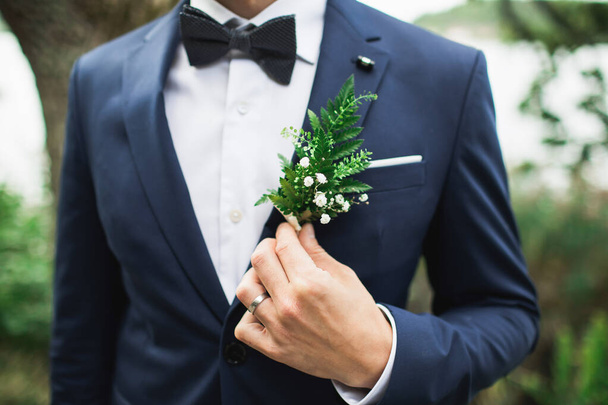 Elegant groom's boutonniere with fern and white flowers. Holding with hand. Forest style. - Foto, afbeelding