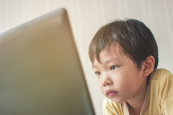 アジアの男の子は家の部屋でノートパソコンの画面を見るのが厳しい. - 写真・画像
