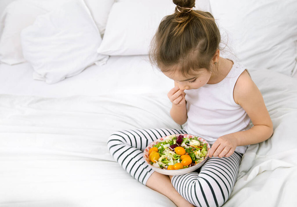 Roztomilá holčička s ovocem a zeleninou na lehkém pozadí. Zdravé jídlo pro děti . - Fotografie, Obrázek