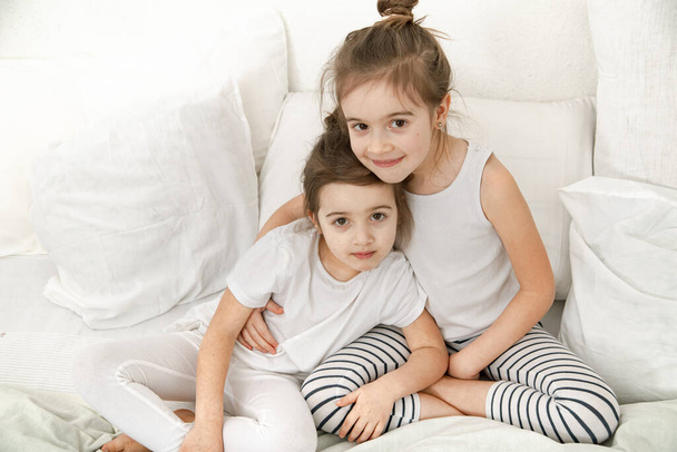 Дві милі дівчинки-сестрички качаються на ліжку в спальні. Концепція сімейних цінностей та дитячої дружби
. - Фото, зображення