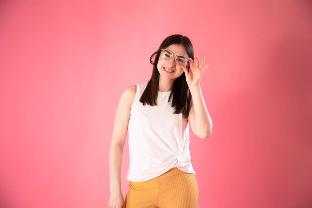 Retrato de una mujer joven mostrando emociones, con gafas sobre un fondo rosa aislado
. - Foto, imagen