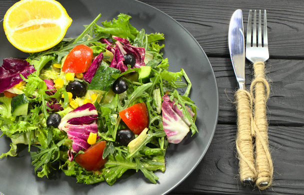Овощной салат на черной тарелке, столовые приборы. Изысканные блюда из рукколы и овощей
. - Фото, изображение