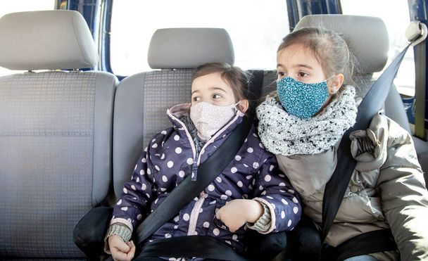 Deux petites filles sont assises dans une voiture sur le siège arrière, portant des masques pendant la pandémie. Virus de la couronne
. - Photo, image
