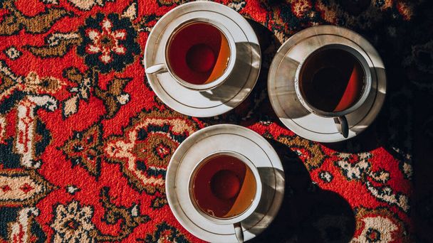 vintage soviet porcelain cups of tea with saucers on turkish carpet, traditional tea ceremony, sunlight - Photo, Image