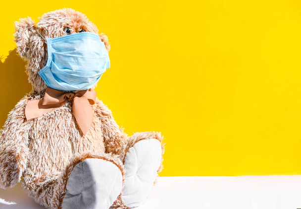 Coronavirus und Luftverschmutzung pm2.5 Konzept. Teddybär in Schutzmaske isoliert auf gelbem Hintergrund mit Kopierraum - Foto, Bild