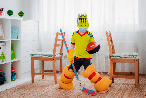 Lapsi poika pelaa jääkiekkoa kotona tehtyään lomakkeen omin käsin improvisoiduista kodin työkaluista ja tuolista valmistetusta portista. Home improvisaatio ja lasten kekseliäisyyttä pelejä kotona. - Valokuva, kuva