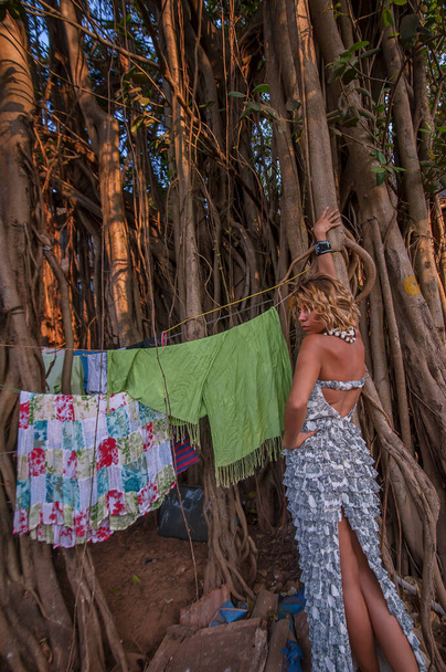 tyttö kauniissa mekossa taustalla vanha iso banian puu poseeraa taustalla pyykkiä
. - Valokuva, kuva