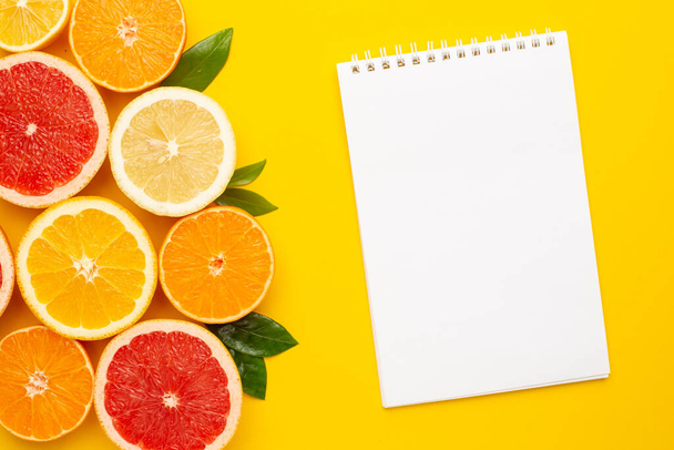 Citruses fruits and notebook on yellow background with copyspace, fruit flatlay, summer minimal compositon with grapefruit, lemon, mandarin and orange top view - Фото, изображение