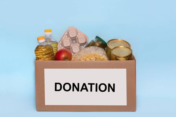 Lebensmittel in einem Spendenkarton, isoliert auf blauem Hintergrund, Kopierraum. Coronavirus-Hilfsfonds und Spenden.Charity-Spenden. Spenden für die Lebensmittelbank - Foto, Bild