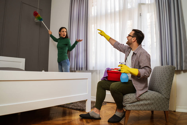 Η γυναίκα είναι θυμωμένη επειδή ο άντρας της είναι τεμπέλης και αποφεύγει να καθαρίσει το διαμέρισμα.. - Φωτογραφία, εικόνα