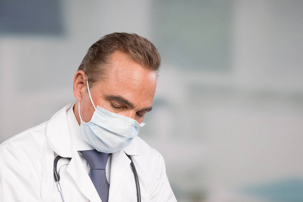 over strained male doctor in lab coat and tie in front of a clinic room - Photo, Image