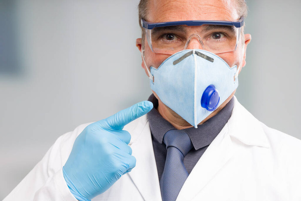 Доктор з медичною маскою для обличчя та медичними рукавичками вказує на його маску
  - Фото, зображення