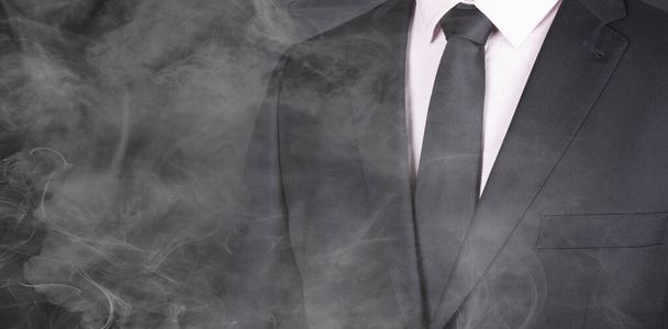 Mies mustassa puvussa ja musta solmio, seisoo savussa, lähikuva
 - Valokuva, kuva