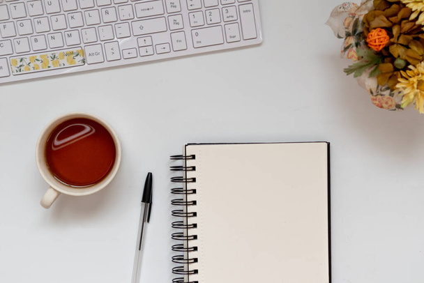 Minimální pracovní prostor: skicák na bílém povrchu s klávesnicí a čajem. Útulná scéna, výhled shora, byt ležel - Fotografie, Obrázek