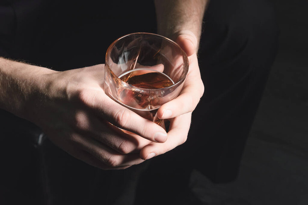 Close-up of the hands of a young man who pours alcohol from a decanter into a glass, on a dark isolated background - Photo, Image