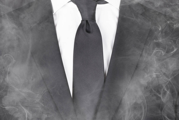Человек в черном костюме и черном галстуке, стоящий в дыму, крупным планом
 - Фото, изображение