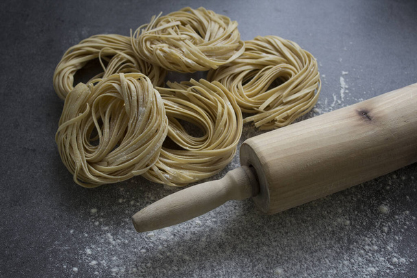 Rohe Pasta Tagliatelle auf dunkelgrauem Hintergrund. Zutaten Foto von oben. Italienische Lebensmittel.  - Foto, Bild