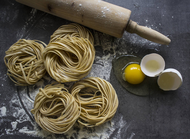 Raw pasta tagliatelle on dark grey background. Ingredients top view photo. Italian food.  - Фото, изображение