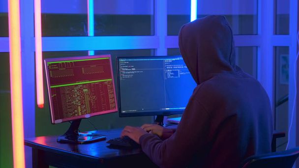 Μέτριο πλάνο του hacker ντυμένος σε ένα σκοτεινό κοντά εργασίας στον υπολογιστή. - Φωτογραφία, εικόνα