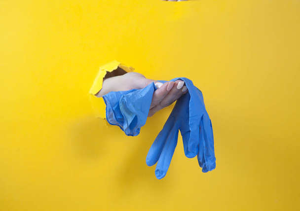 Female hand holds blue rubber gloves on a yellow background. Hand in the hole. Hygiene. Purity. covtd-19 - Foto, Imagem