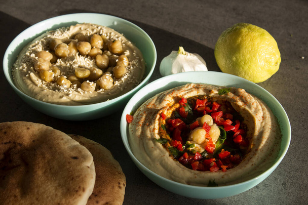 Koyu gri masada iki farklı humus türü var. Masada pita ekmeği olan taze ev yapımı humus tabağı. Ortadoğu 'nun otantik yemekleri. Sağlıklı beslenme konsepti. Vejetaryen dengeli yemek. İsrail 'in geleneksel yemeği.  - Fotoğraf, Görsel