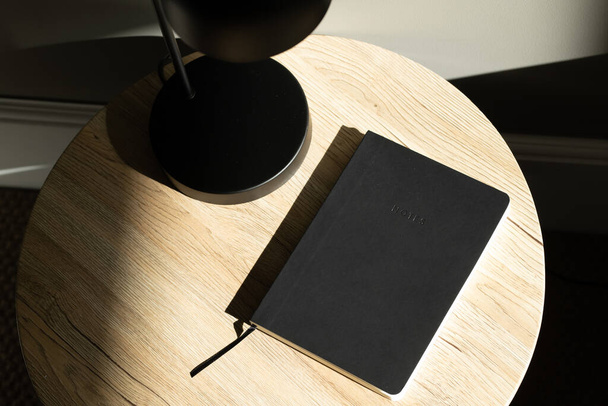 Черная лампа и черная книга на столе с солнечным светом возле кровати
. - Фото, изображение