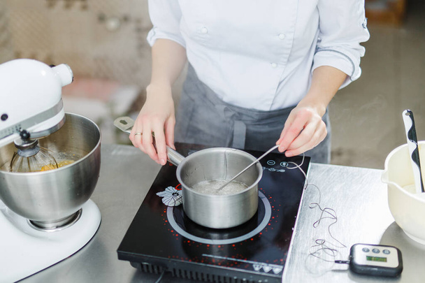 Woman in white uniform prepares food in a professional kitchen - Foto, afbeelding