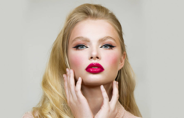 Woman. Face close up. Cosmetics - raspberry lipstick, blush, eyeliner. Fingers near the chin. - Фото, изображение