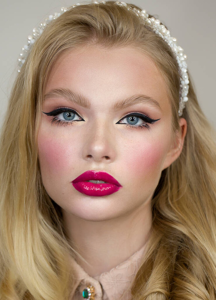 Woman's face close up. Beauty portrait. Bright makeup, pink lips, long bunches of eyelashes on the lower eyelid and black arrows. She somtrit straight. Clean and healthy skin. Blush on cheeks. Blonde hair. - Foto, imagen
