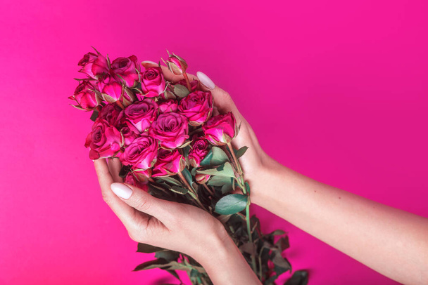 Woman's hand holding beautiful bouquet of pink roses flowers on bright pink background, flat lay. Flowers bouquet in hands - Fotó, kép