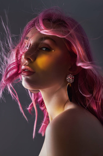 Art beauty portrait of a woman with pink hair, creative coloring. Bright colored highlights and shadows on the face, a girl with jewelry. Dyed hair in the wind - Photo, Image