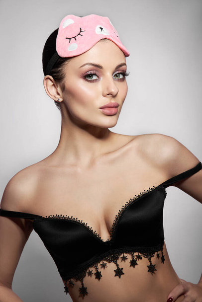 Beauty portrait of a Woman with a sleep mask and pink delicate makeup on her lips and eyes. Sexy brunette girl in underwear - Photo, image
