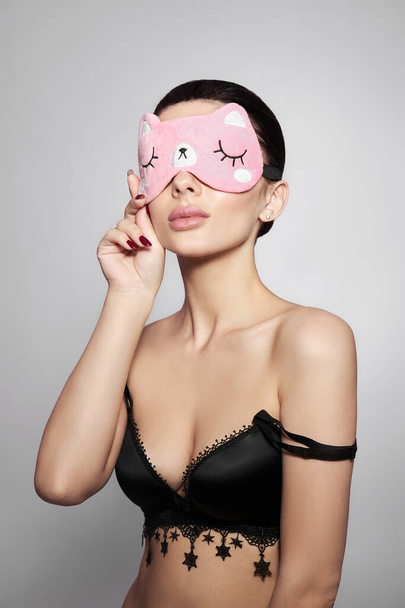 Beauty portrait of a Woman with a sleep mask and pink delicate makeup on her lips and eyes. Sexy brunette girl in underwear - Foto, imagen