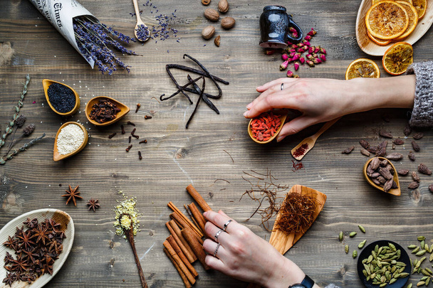 Különböző fűszerek, gyógynövények és gyökerek felülről. Rusztikus háttérrel. Női kezek néhányat. - Fotó, kép